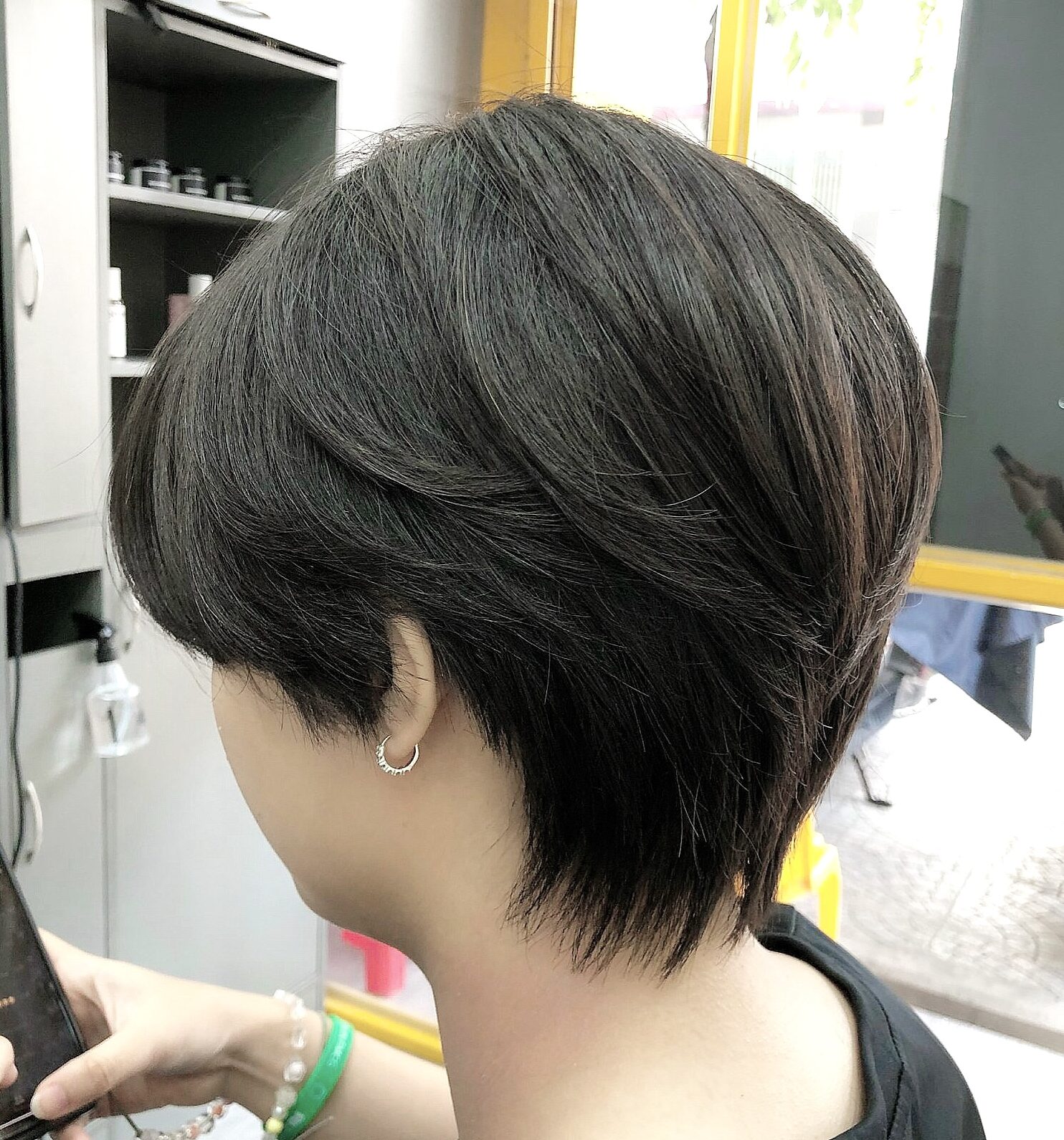 Tóc ngắn đen tỉa layer ôm đầu và gáy, nhìn nghiêng từ phía sau.