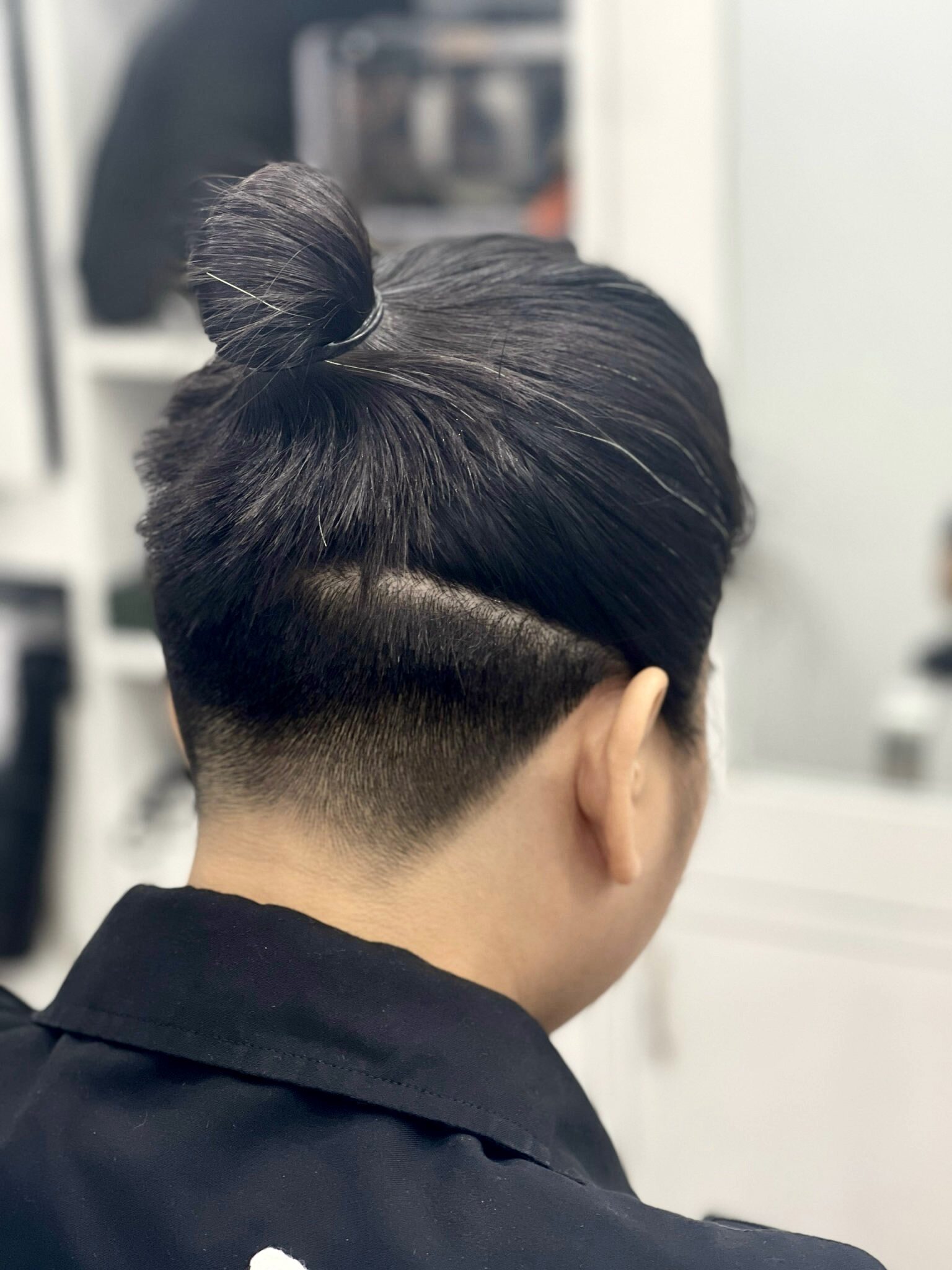 Tóc undercut cắt sát gáy, phần tóc dài phía trên buộc búi, nhìn từ phía sau.